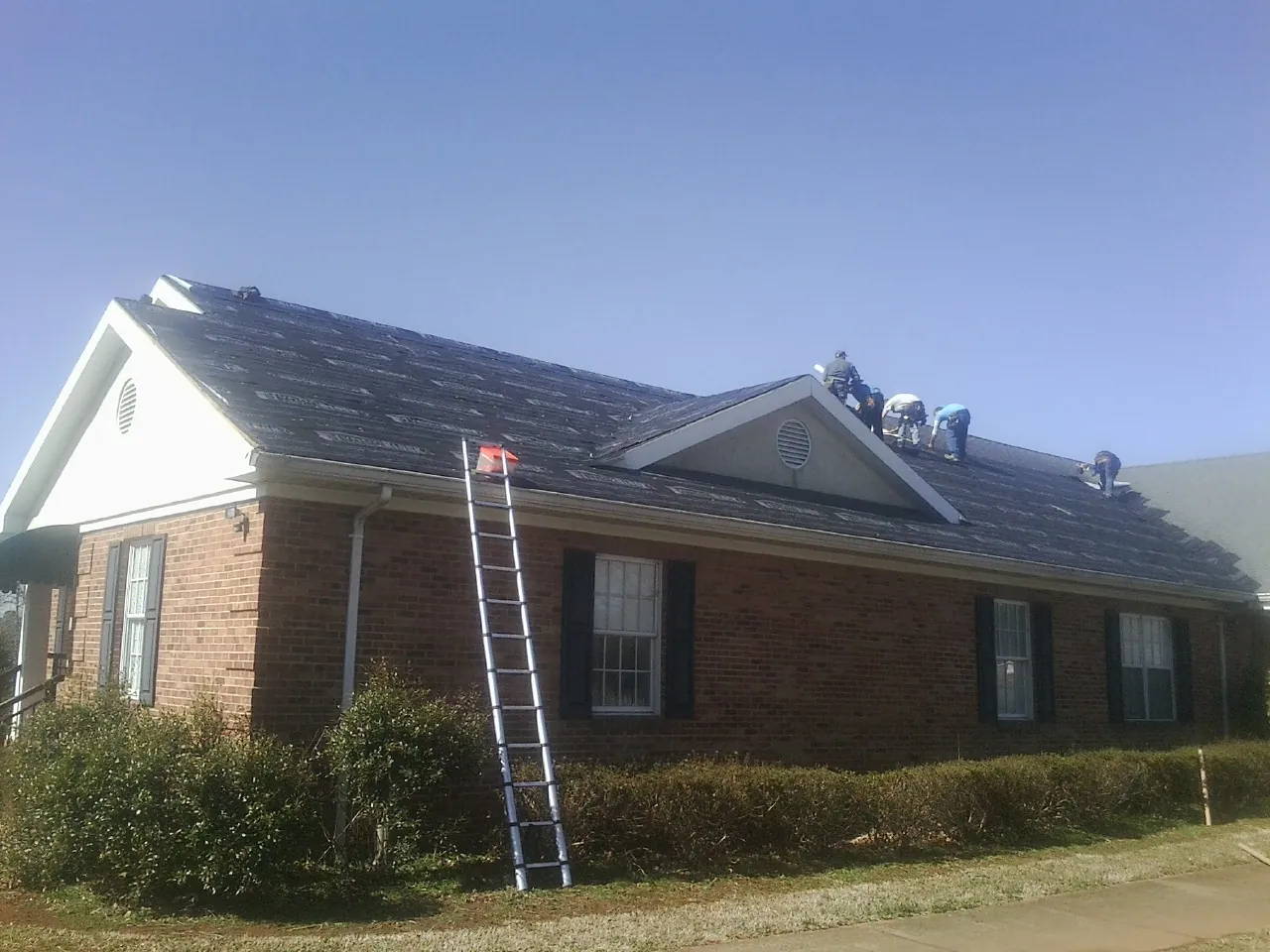 Crew tearing shingles off a brick ranch roof with a ladder set — Metal Roof Repair work by our crew in Cobbs Creek