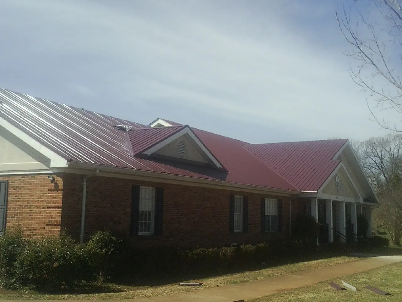 Red metal roof with gabled entries on a long brick building, from a Hail Damage Roof Repair job in Cobbs Creek