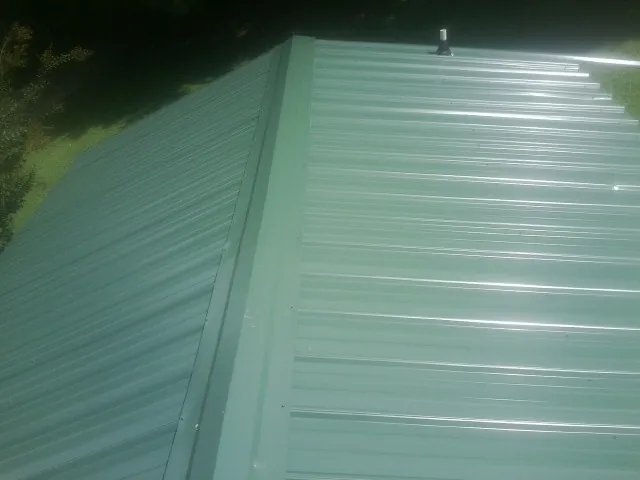 New green metal panels meeting at the ridge of a roof — Flat Roof Repair work by our crew in Cobbs Creek