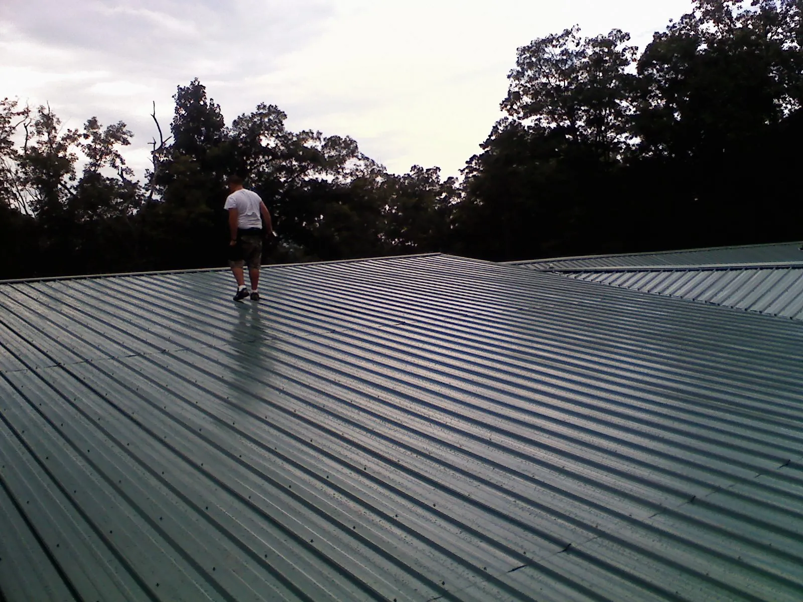 Roofer walking a wide expanse of new green metal roofing in Cobbs Creek