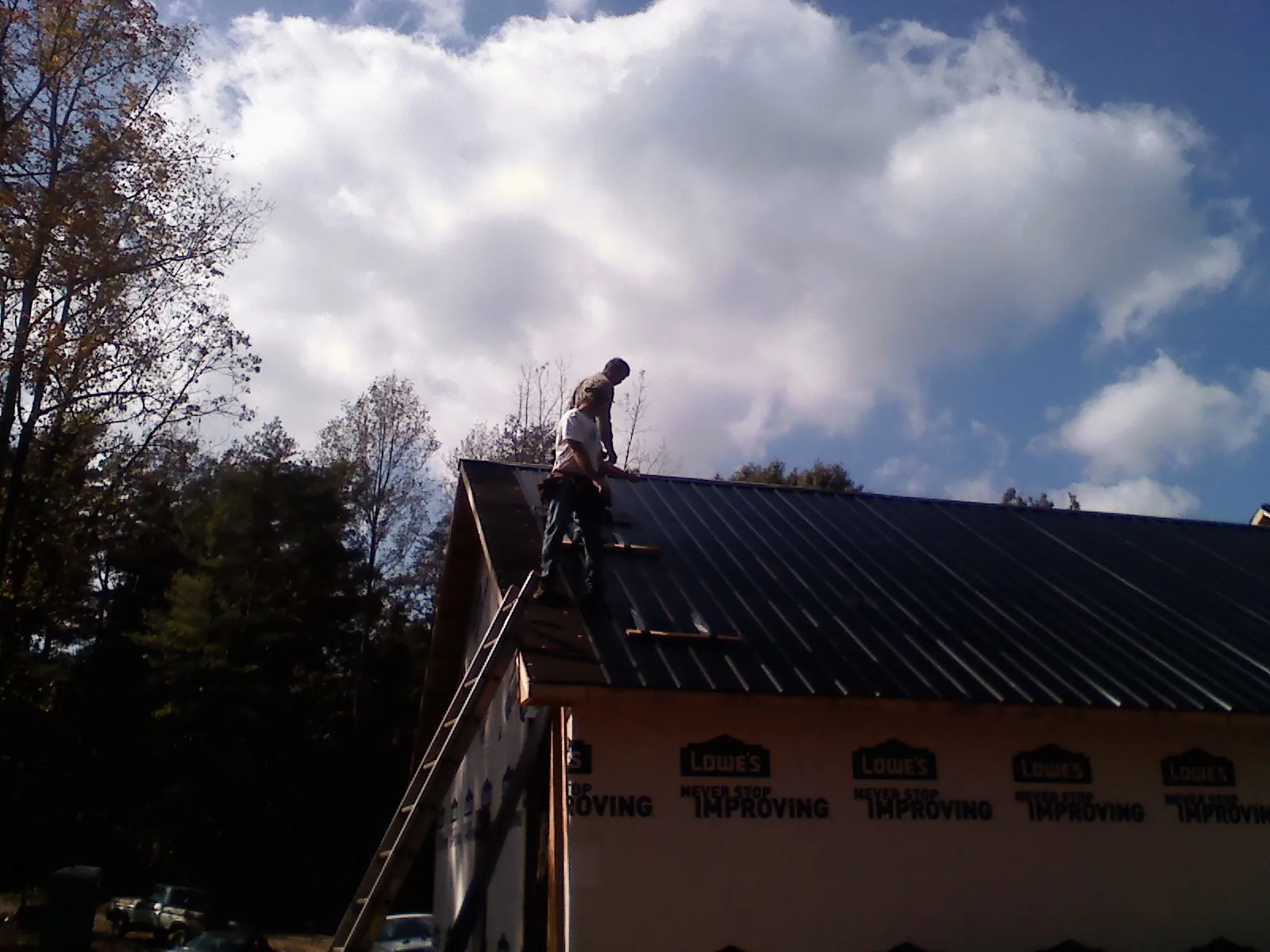 Roofer fastening dark metal panels high against a cloudy sky, from a Roof Inspection job in Cobbs Creek