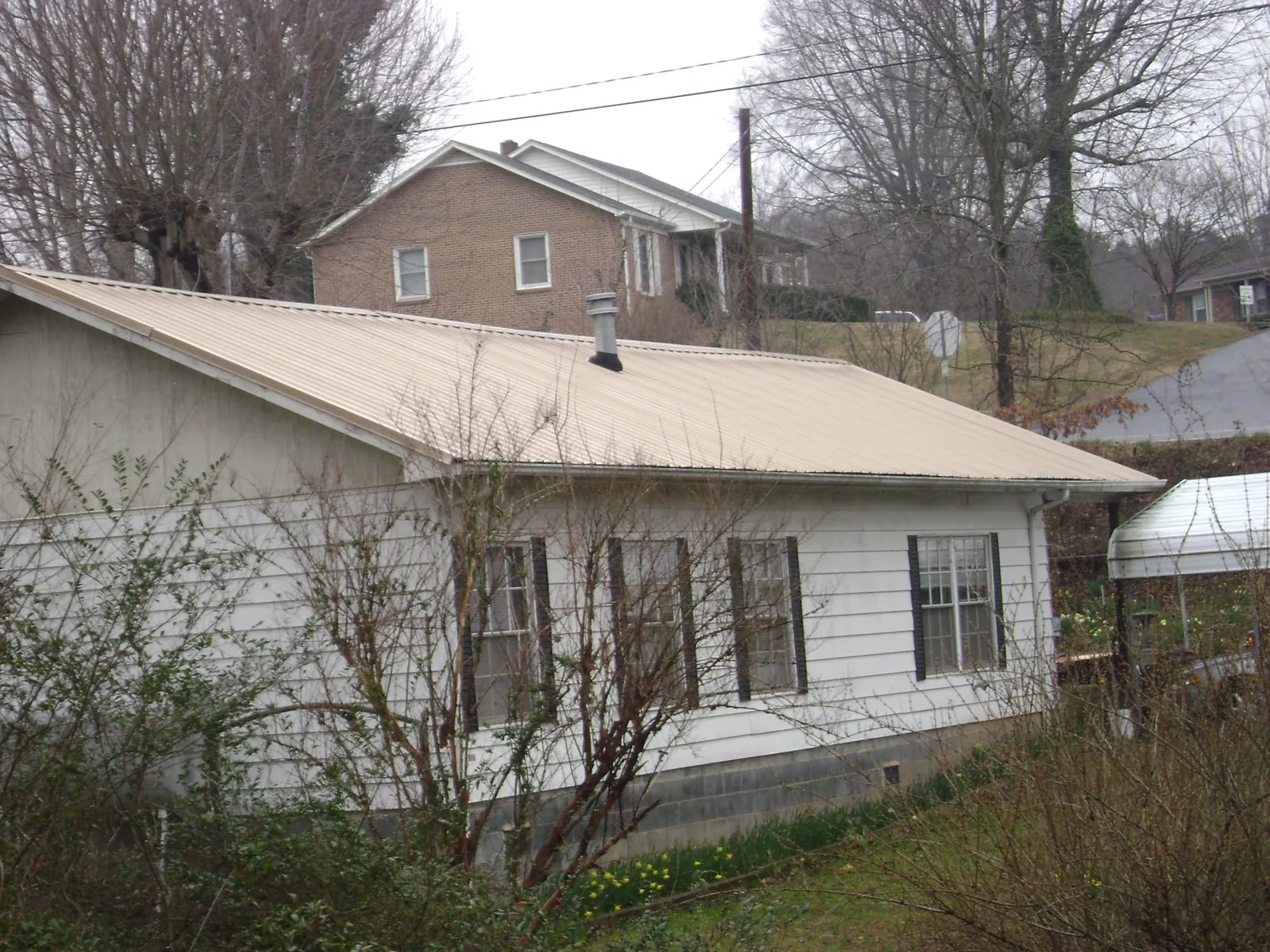 Tan metal roof on a white sided house set into a hillside — Commercial Roofing by Roofing Brothers in Cobbs Creek