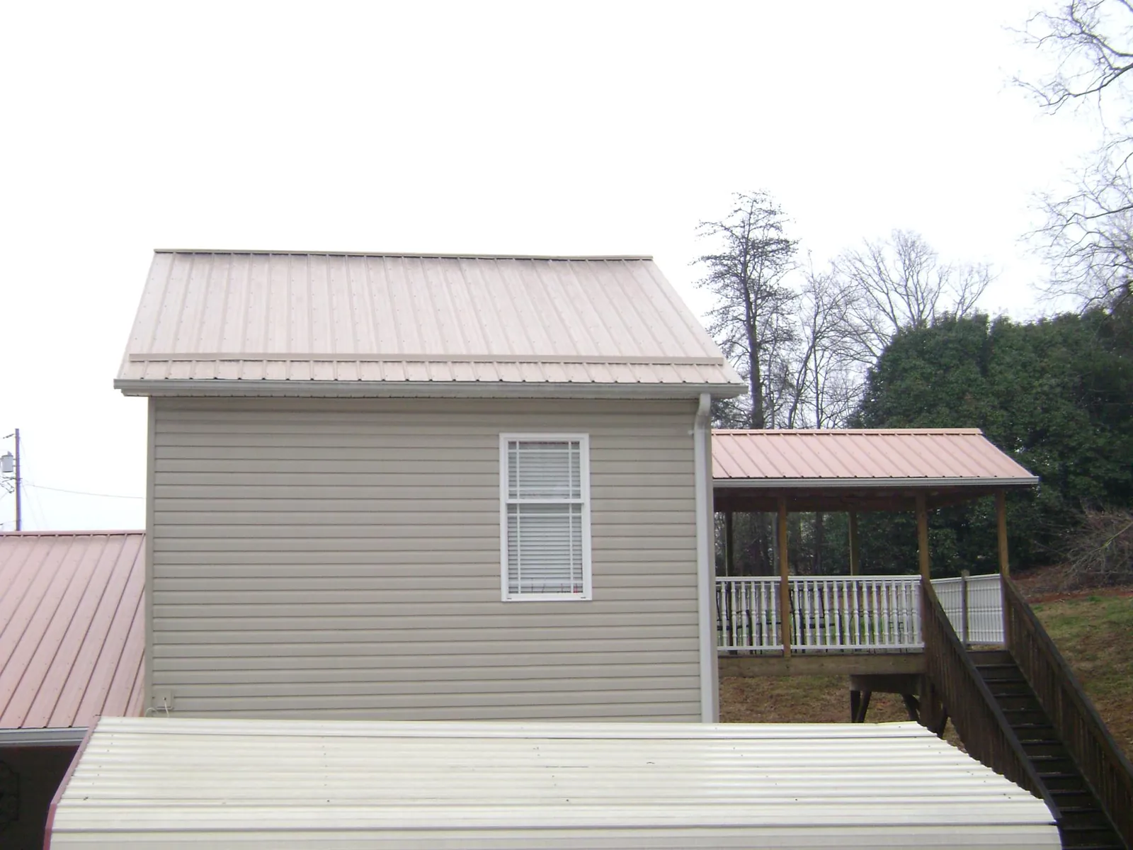 Tan metal roofs on a two story addition and attached porch, from a Roof Replacement job in Cobbs Creek